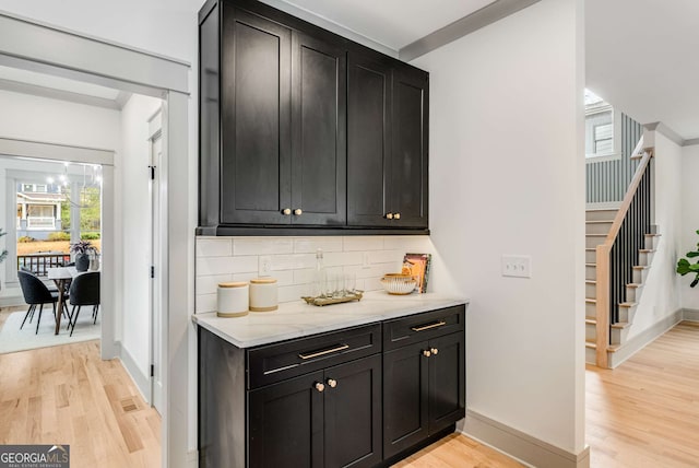 bar with tasteful backsplash, light stone countertops, and light wood-type flooring