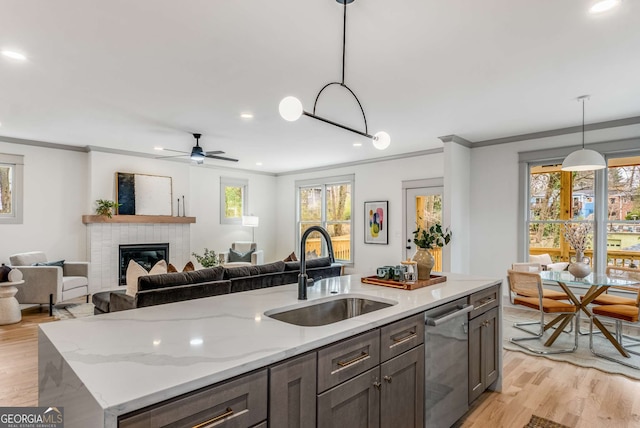 kitchen featuring sink, dishwasher, a kitchen island with sink, light stone counters, and decorative light fixtures