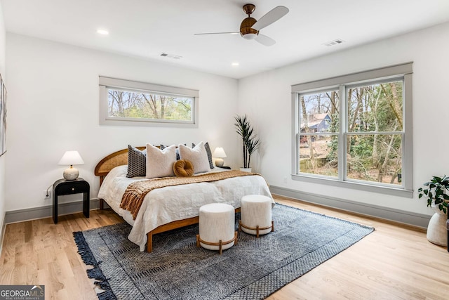 bedroom featuring ceiling fan, light hardwood / wood-style floors, and multiple windows