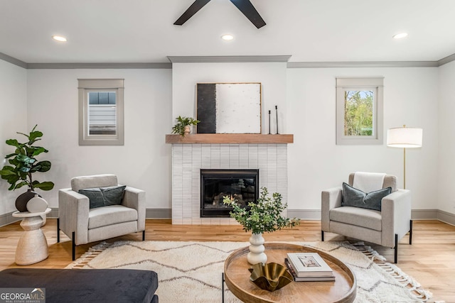 living room with ceiling fan, ornamental molding, wood-type flooring, and a tiled fireplace