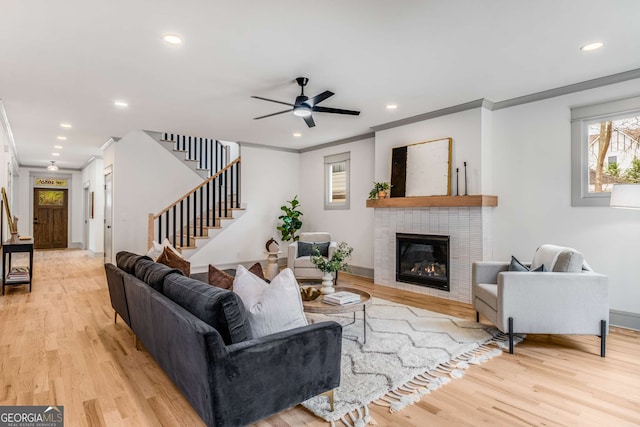 living room featuring a tiled fireplace, ornamental molding, ceiling fan, and light hardwood / wood-style floors