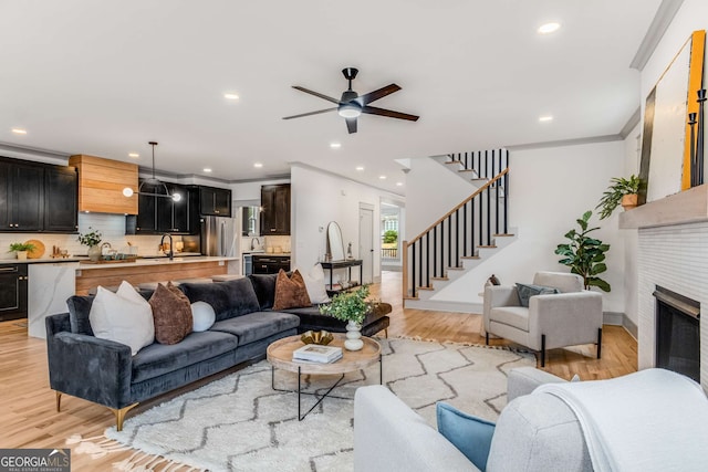 living room featuring ornamental molding, sink, ceiling fan, and light wood-type flooring