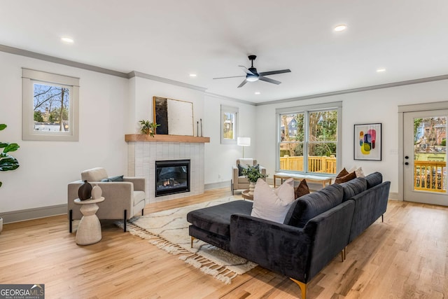 living room featuring a tile fireplace, ornamental molding, a wealth of natural light, and light wood-type flooring