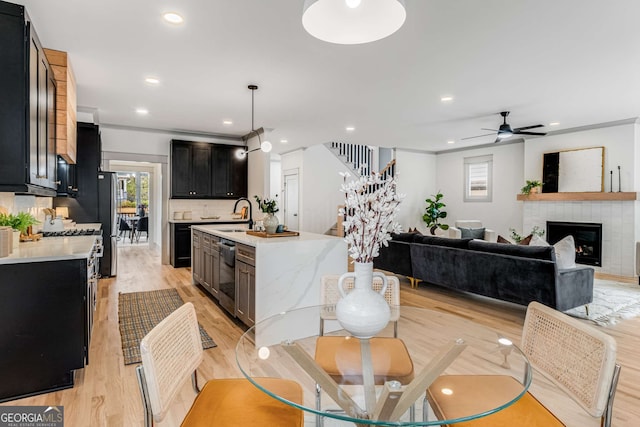 kitchen featuring a tile fireplace, stainless steel appliances, light hardwood / wood-style floors, decorative backsplash, and decorative light fixtures