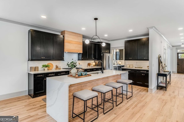 kitchen featuring appliances with stainless steel finishes, hanging light fixtures, a center island with sink, a kitchen bar, and light wood-type flooring