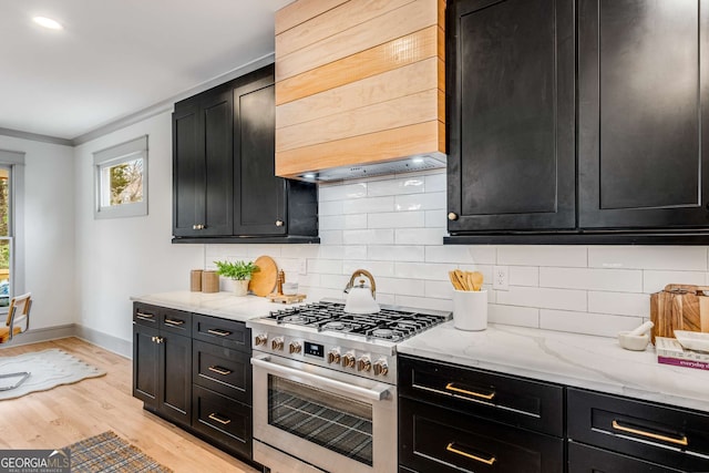 kitchen with backsplash, high end stainless steel range, light wood-type flooring, and light stone counters