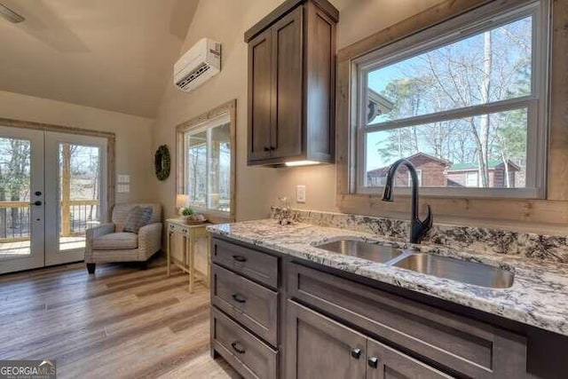 kitchen featuring sink, a wall mounted AC, light stone countertops, light hardwood / wood-style floors, and french doors