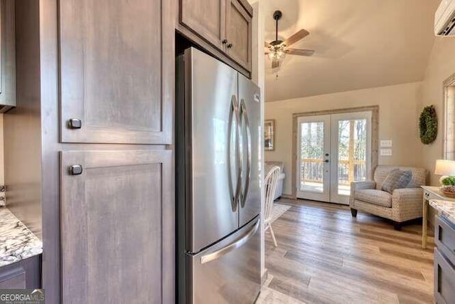 kitchen with french doors, lofted ceiling, light wood-type flooring, stainless steel fridge, and light stone countertops