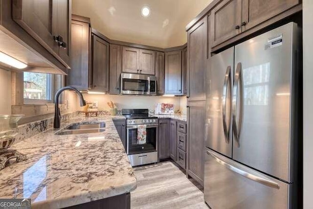 kitchen with dark brown cabinetry, sink, light stone countertops, and appliances with stainless steel finishes