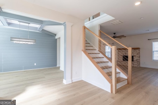 stairway featuring ceiling fan, lofted ceiling with beams, a stone fireplace, wood finished floors, and baseboards