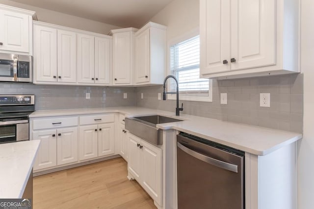 kitchen featuring light countertops, appliances with stainless steel finishes, light wood-style floors, white cabinetry, and a sink