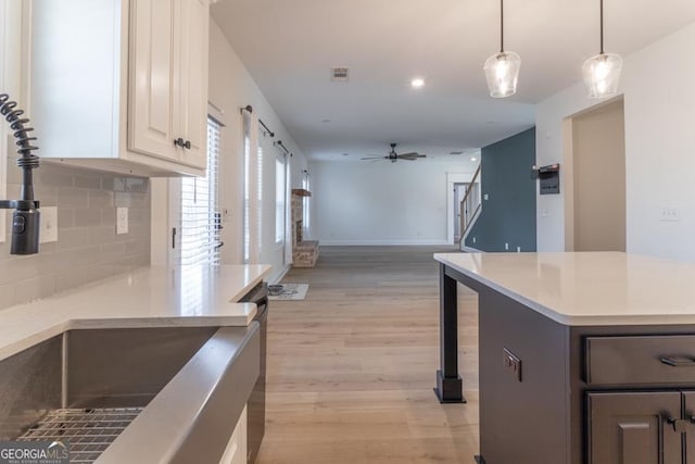 kitchen with ceiling fan, light wood-style flooring, open floor plan, light countertops, and decorative backsplash