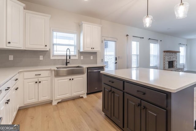 kitchen with light wood finished floors, dishwasher, open floor plan, white cabinetry, and a sink