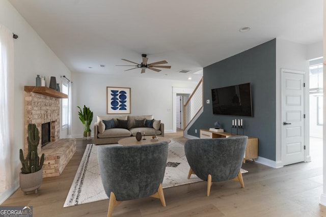 living area with baseboards, visible vents, a fireplace with raised hearth, wood finished floors, and stairs