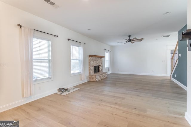 unfurnished living room featuring a fireplace, visible vents, stairway, light wood-style floors, and a ceiling fan