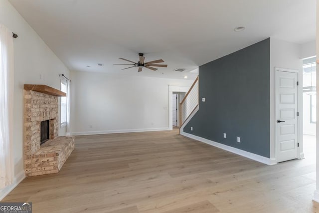 unfurnished living room featuring light wood finished floors, a brick fireplace, and stairway