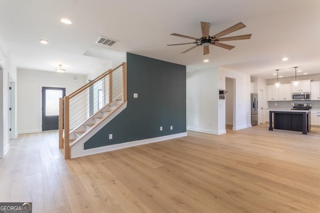 unfurnished living room featuring visible vents, baseboards, light wood-style flooring, stairs, and recessed lighting