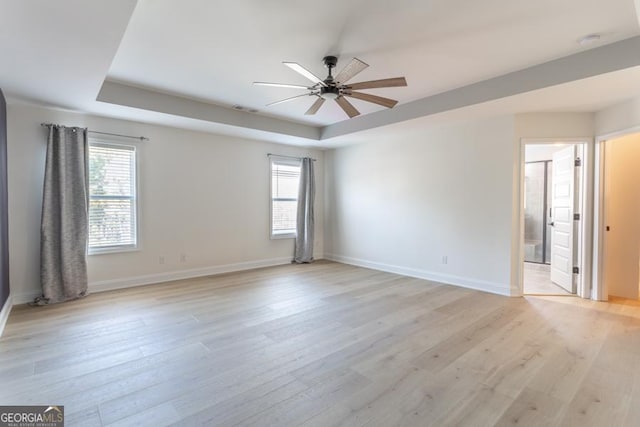 spare room featuring visible vents, baseboards, ceiling fan, a tray ceiling, and light wood-type flooring