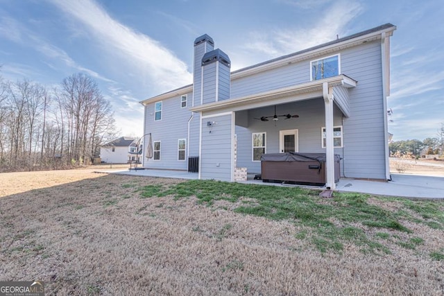 back of house featuring a ceiling fan, a lawn, a chimney, a patio area, and a hot tub