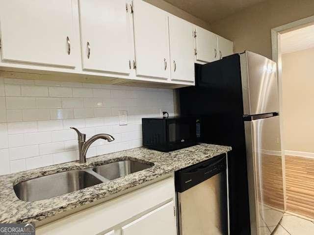 kitchen with sink, white cabinetry, stainless steel dishwasher, light stone countertops, and decorative backsplash