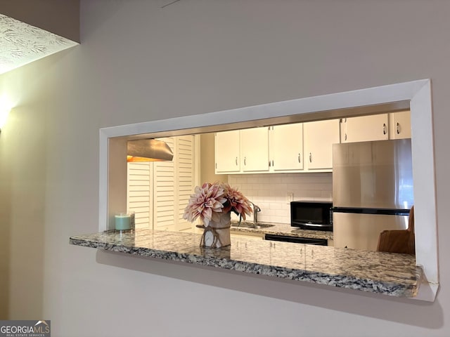 kitchen featuring sink, stainless steel refrigerator, white cabinetry, tasteful backsplash, and light stone countertops