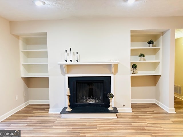 unfurnished living room with light hardwood / wood-style floors, built in features, and a textured ceiling