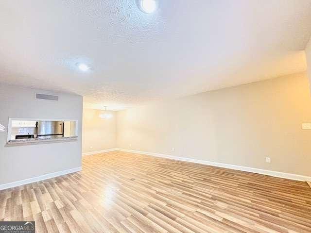 unfurnished living room with a textured ceiling and light hardwood / wood-style floors