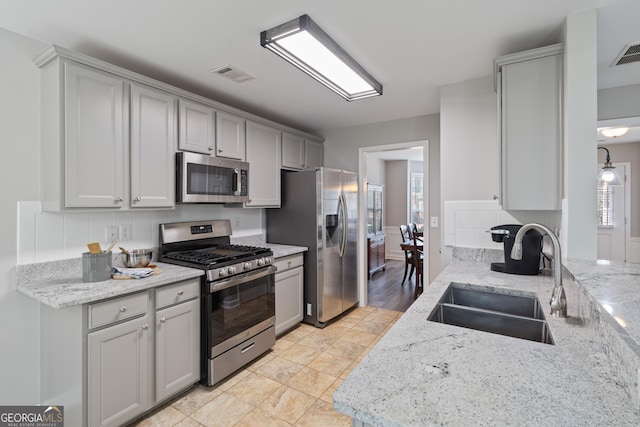 kitchen with stainless steel appliances, light stone countertops, sink, and gray cabinetry