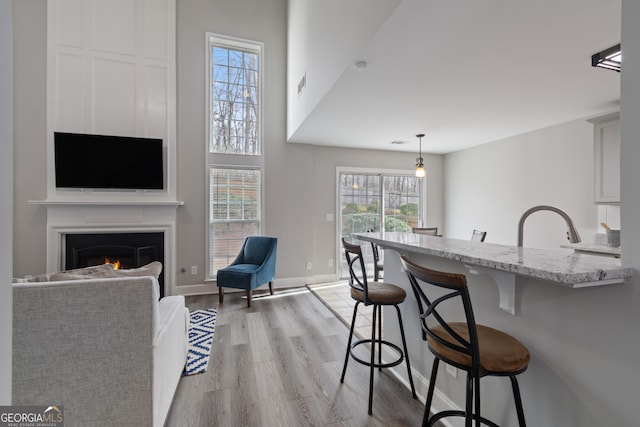 kitchen featuring a breakfast bar area, light stone counters, hanging light fixtures, light wood-type flooring, and white cabinets