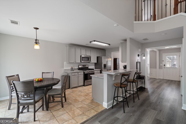 kitchen with gray cabinets, pendant lighting, a breakfast bar area, stainless steel appliances, and light stone countertops