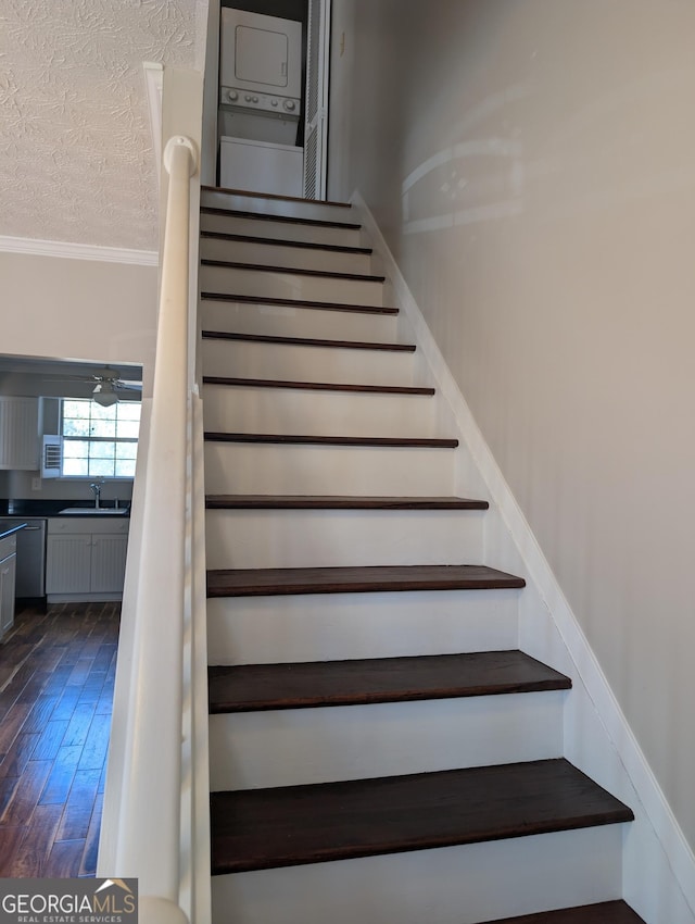 stairway featuring sink, stacked washer / dryer, wood-type flooring, ornamental molding, and a textured ceiling