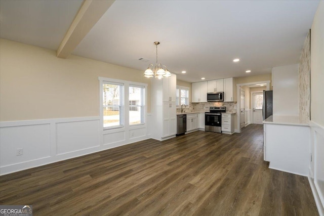 kitchen with decorative light fixtures, appliances with stainless steel finishes, white cabinets, beam ceiling, and backsplash