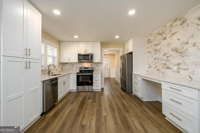 kitchen with sink, appliances with stainless steel finishes, built in desk, white cabinets, and decorative backsplash