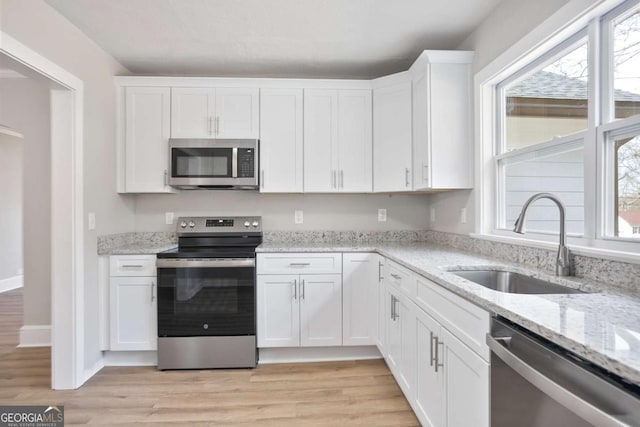 kitchen featuring sink, stainless steel appliances, light stone countertops, light hardwood / wood-style floors, and white cabinets