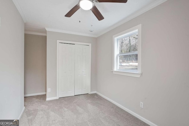 unfurnished bedroom featuring ornamental molding, light colored carpet, ceiling fan, and a closet