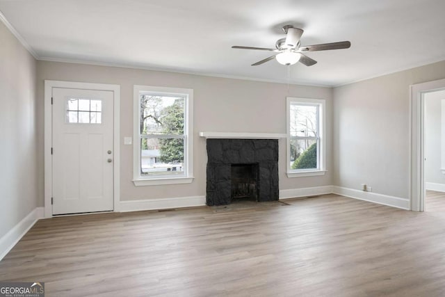 unfurnished living room with crown molding, ceiling fan, a stone fireplace, and light wood-type flooring