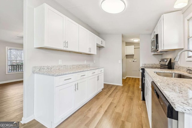 kitchen with light stone counters, stainless steel appliances, sink, and white cabinets