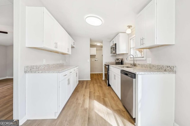 kitchen featuring sink, white cabinetry, light hardwood / wood-style flooring, stainless steel appliances, and light stone countertops