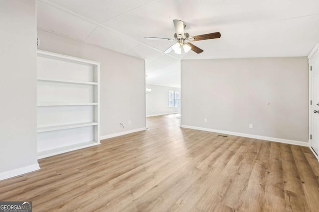 unfurnished living room featuring built in shelves, vaulted ceiling, ceiling fan, and light wood-type flooring