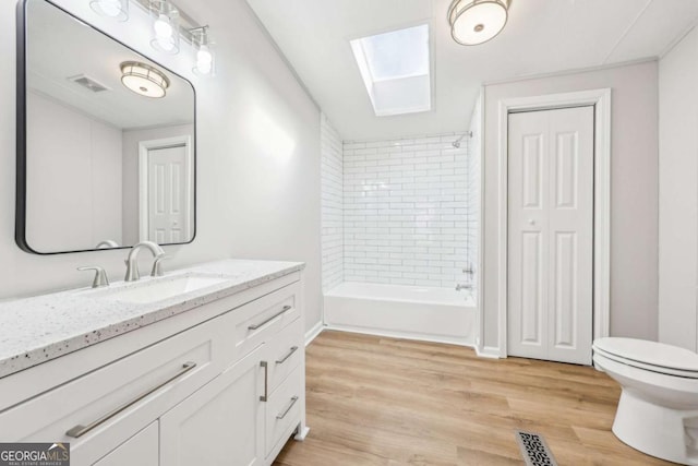 full bathroom featuring a skylight, wood-type flooring, tiled shower / bath combo, vanity, and toilet