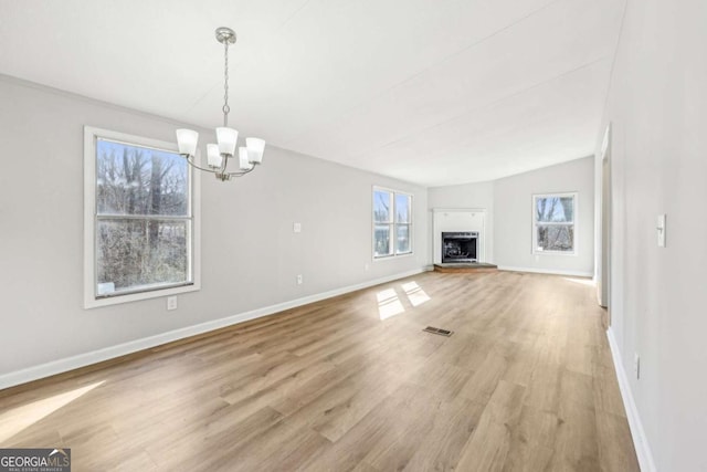 unfurnished living room with an inviting chandelier, a healthy amount of sunlight, vaulted ceiling, and light wood-type flooring