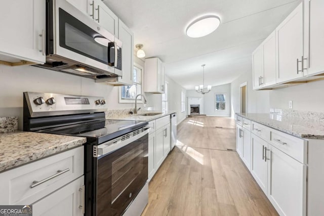 kitchen with lofted ceiling, sink, white cabinetry, light wood-type flooring, and appliances with stainless steel finishes