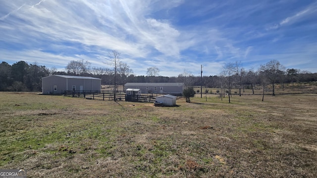 view of yard featuring a rural view, fence, a pole building, and an outbuilding