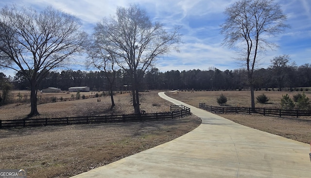 view of property's community with a rural view, fence, and a wooded view