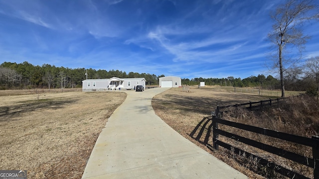 view of yard featuring a rural view, an outdoor structure, fence, a detached garage, and concrete driveway