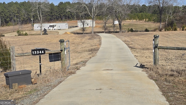 view of street featuring concrete driveway, a rural view, and a gated entry