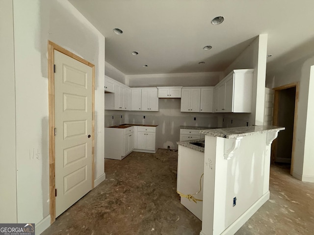 150 Asa Moseley Rd, Mcdonough, GA 30252 - kitchen featuring a peninsula, a kitchen bar, concrete floors, stone counters, and white cabinetry