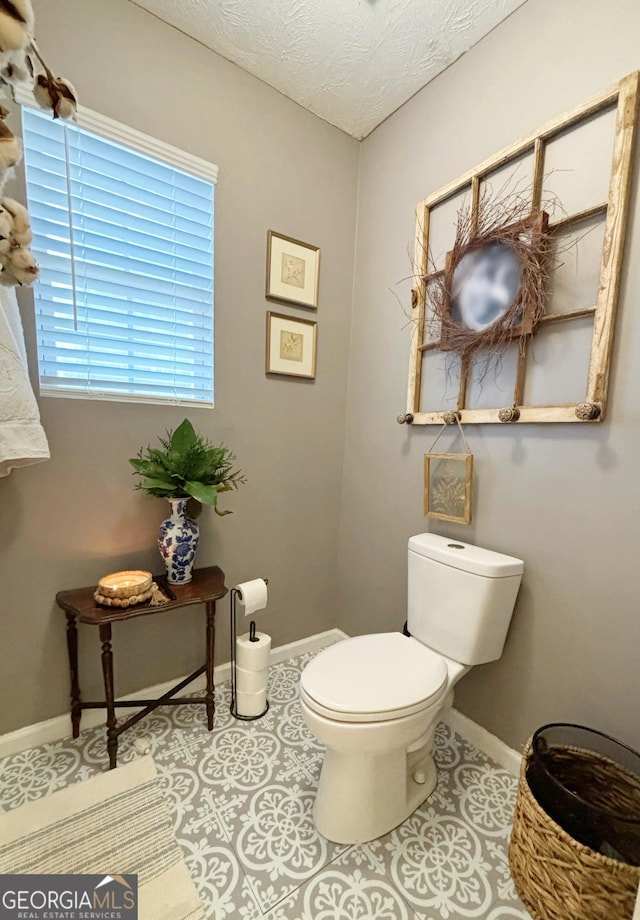 bathroom with a healthy amount of sunlight, toilet, tile patterned flooring, and a textured ceiling