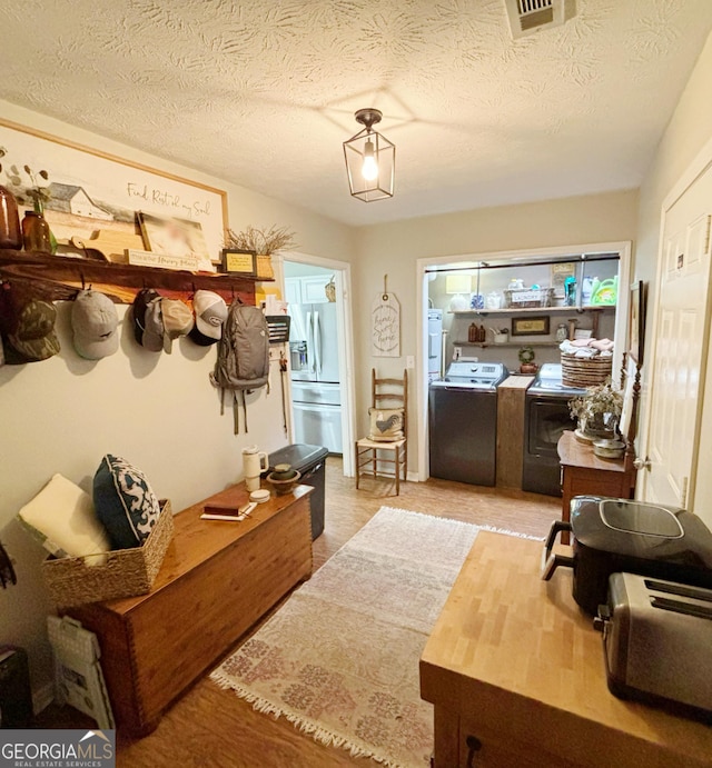 mudroom featuring washer / dryer, a textured ceiling, and light wood-type flooring