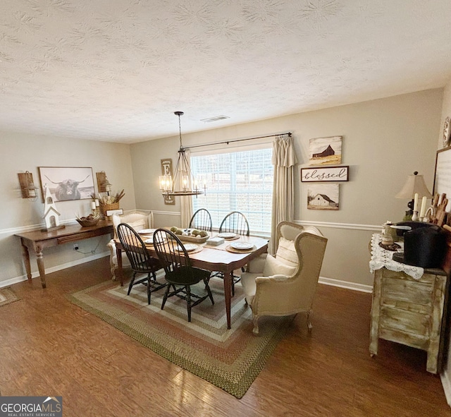 dining area with dark wood-type flooring, a notable chandelier, and a textured ceiling